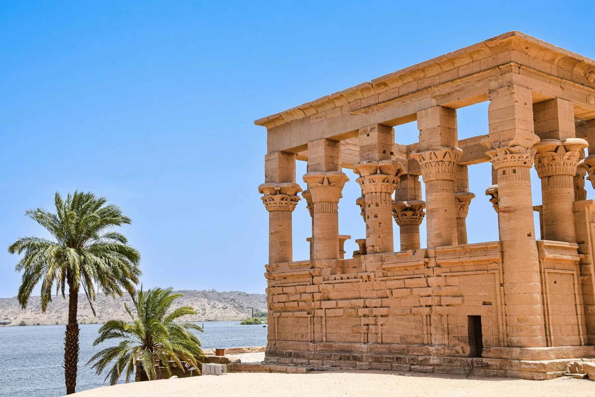 Columnas de un quiosco del templo de Philae, con palmeras y el Nilo al fondo